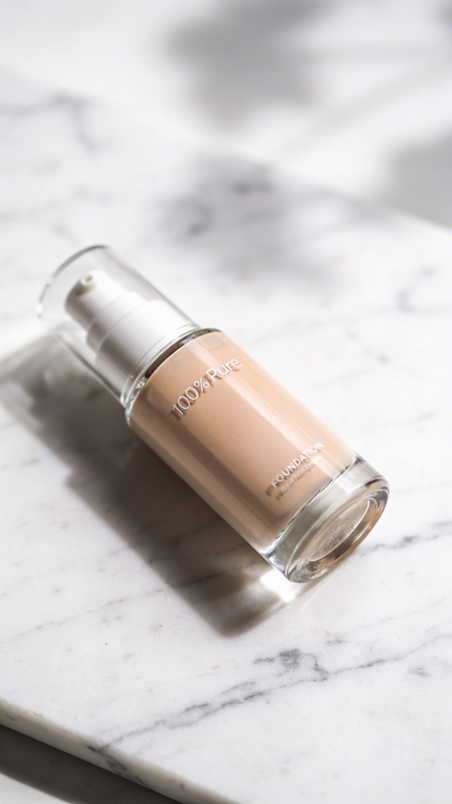 100% Pure foundation bottle on white marble, natural light